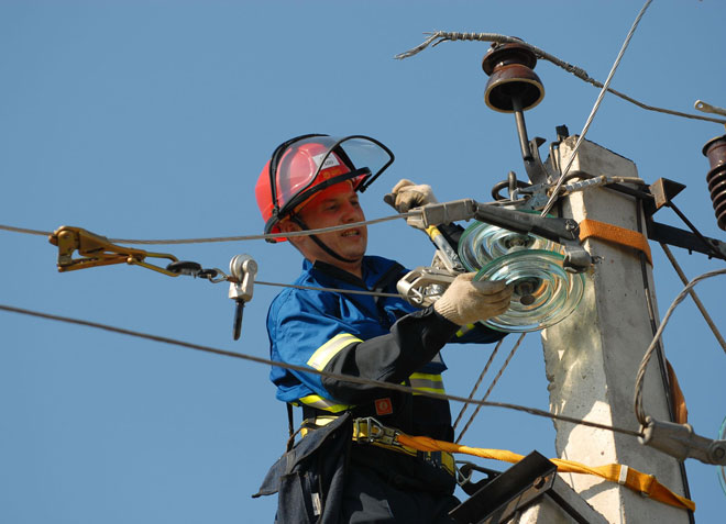 Un electrician instalează izolatori pe un stâlp. 